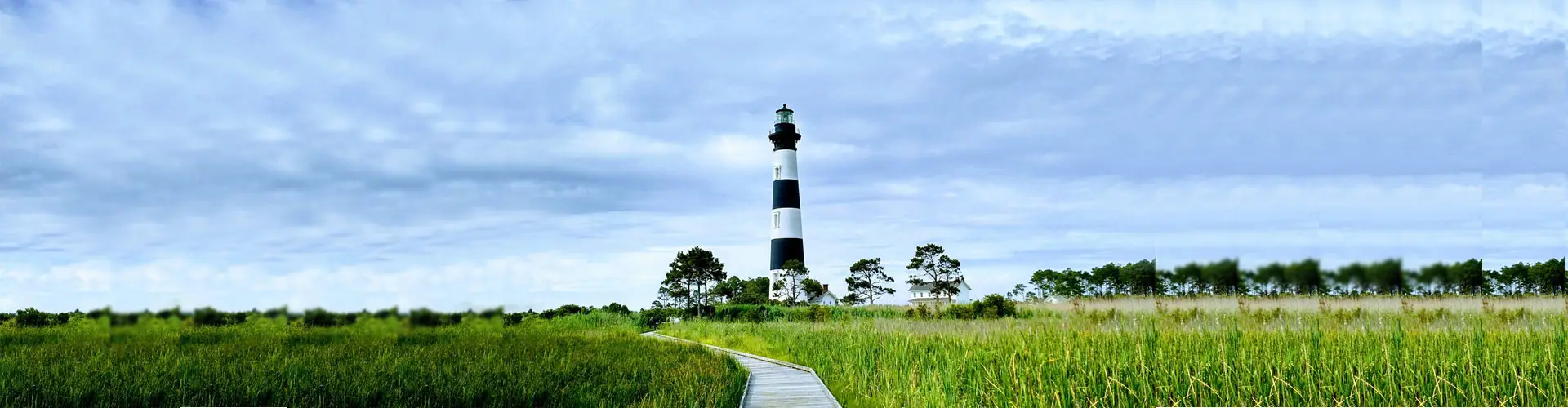Bodie Island Lighthouse in its black and white bands at the end of a boardwalk across bright green marsh grass