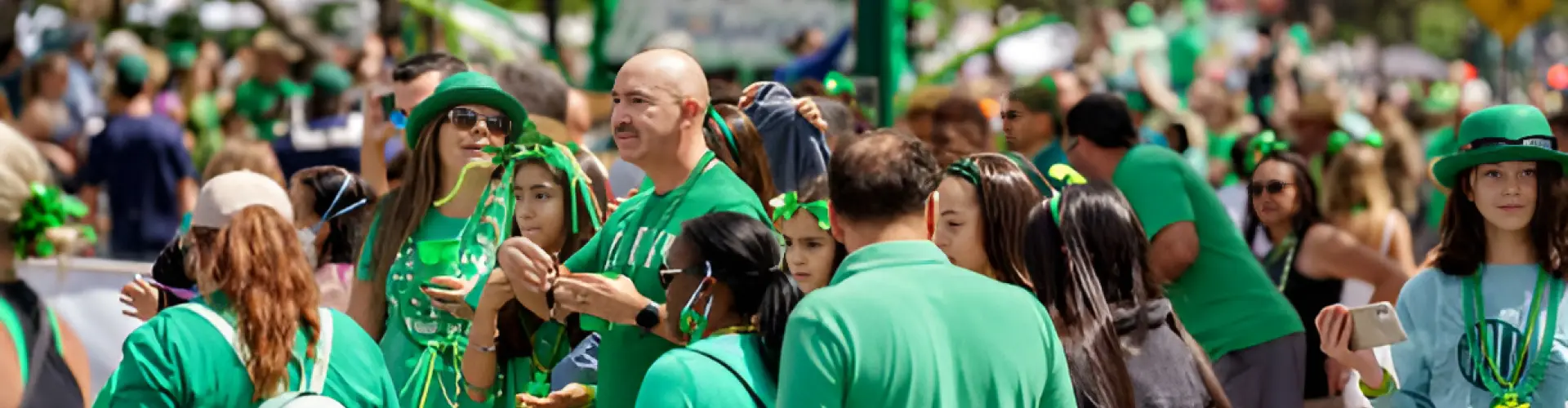 A crowd dressed head to toe in green, in shamrock hats and beads, packed shoulder to shoulder