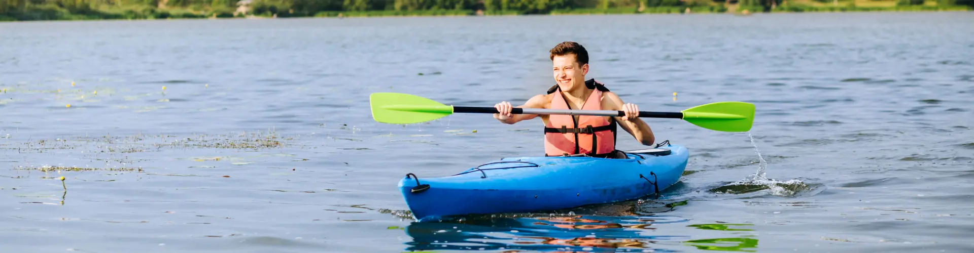 A man in a life vest paddling a blue inflatable kayak across flat open water
