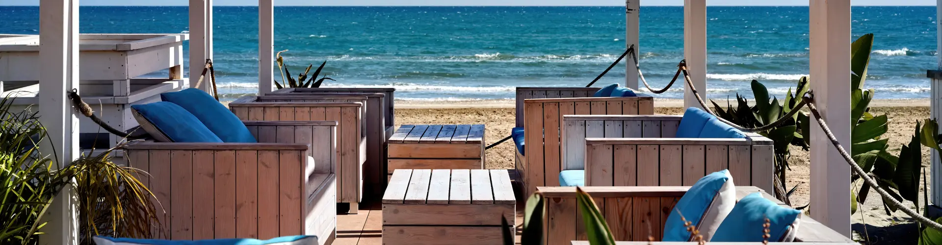 A beachfront lounge deck of pale timber sofas with blue cushions, looking straight out to deep blue sea