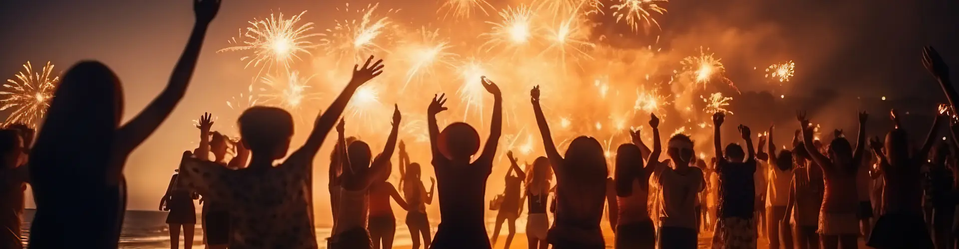 A crowd in silhouette with arms raised as golden fireworks burst overhead