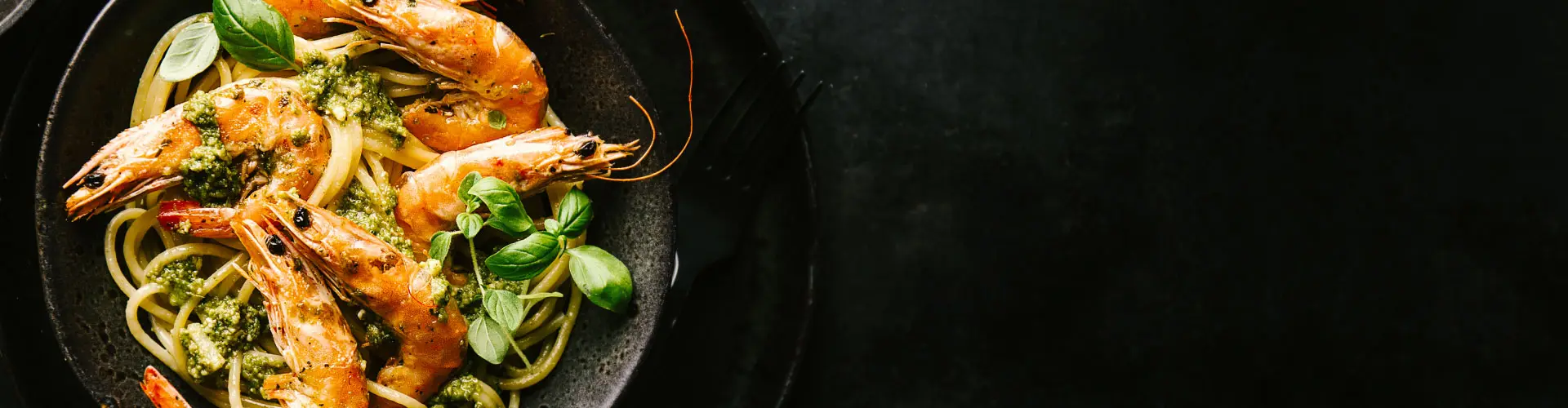 A pan of prawns and linguine scattered with herbs and chilli on a dark table