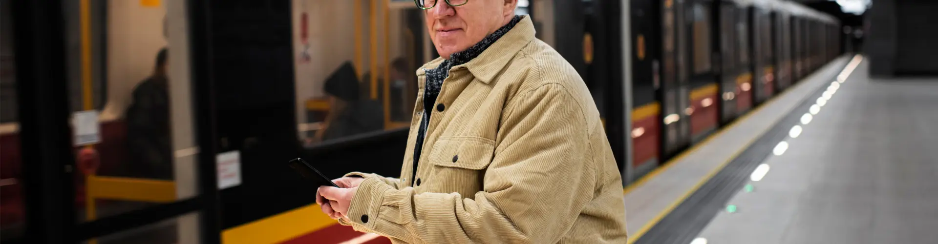 An older man in a beige jacket waiting alone beside a train on an underground platform