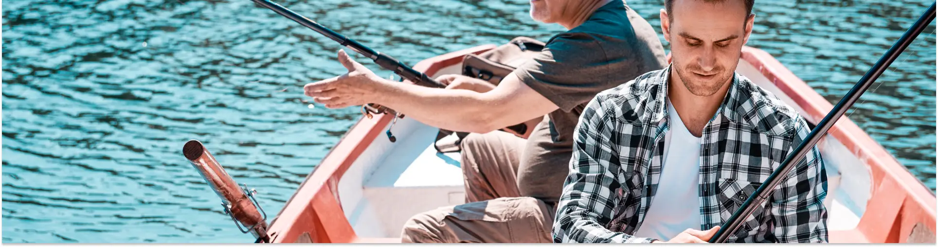 Two men fishing from a small rowing boat on clear turquoise water, one pointing out across it