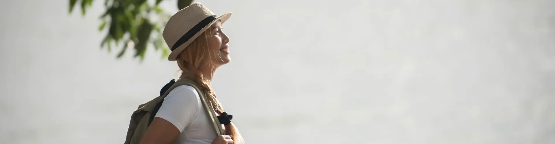 A woman in a straw sun hat with a backpack, turned away into bright washed-out light