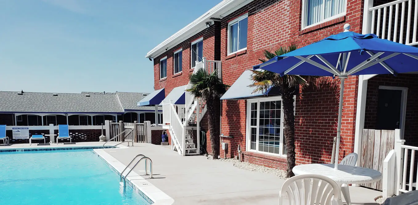 The Colonial Inn Motel outdoor pool, with a blue parasol and the red-brick building behind it