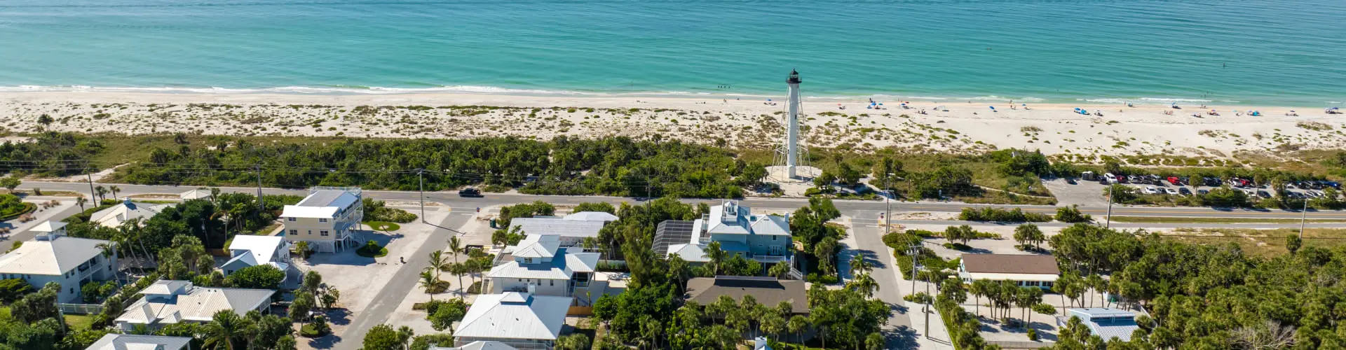 An aerial of a low village of houses among trees on a narrow strip of land, a lighthouse tower among them