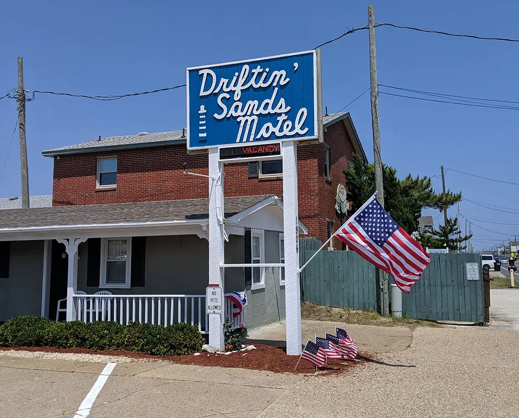 The Driftin' Sands Motel roadside sign in blue and white, beside the porch and an American flag