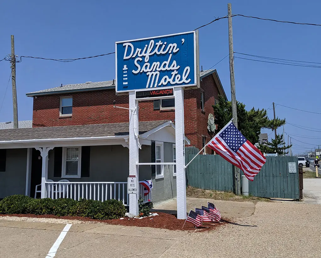The Driftin' Sands Motel roadside sign in blue and white, beside the porch and an American flag