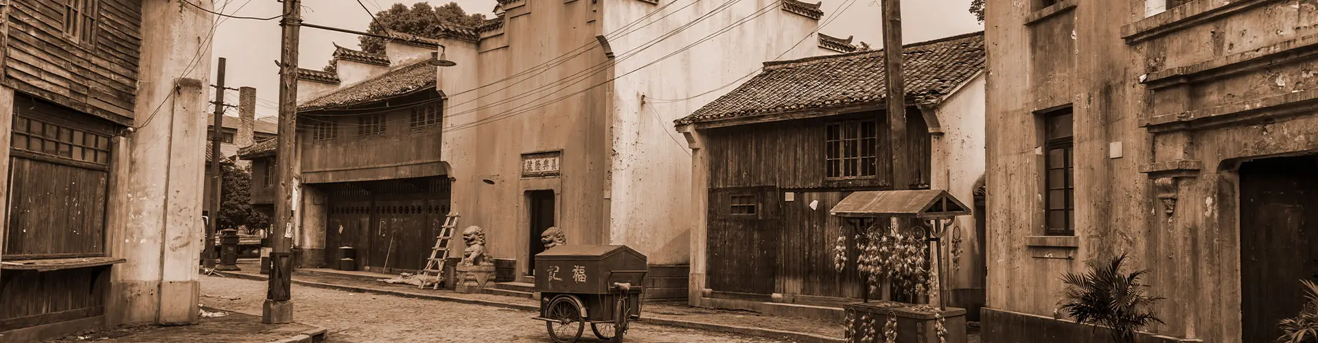 A sepia photograph of a dirt street running between weathered wooden storefronts in an old village