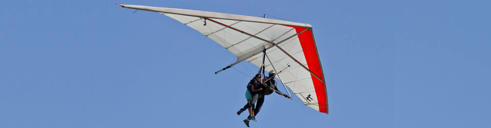A hang glider beneath a red and white wing hanging in an empty blue sky