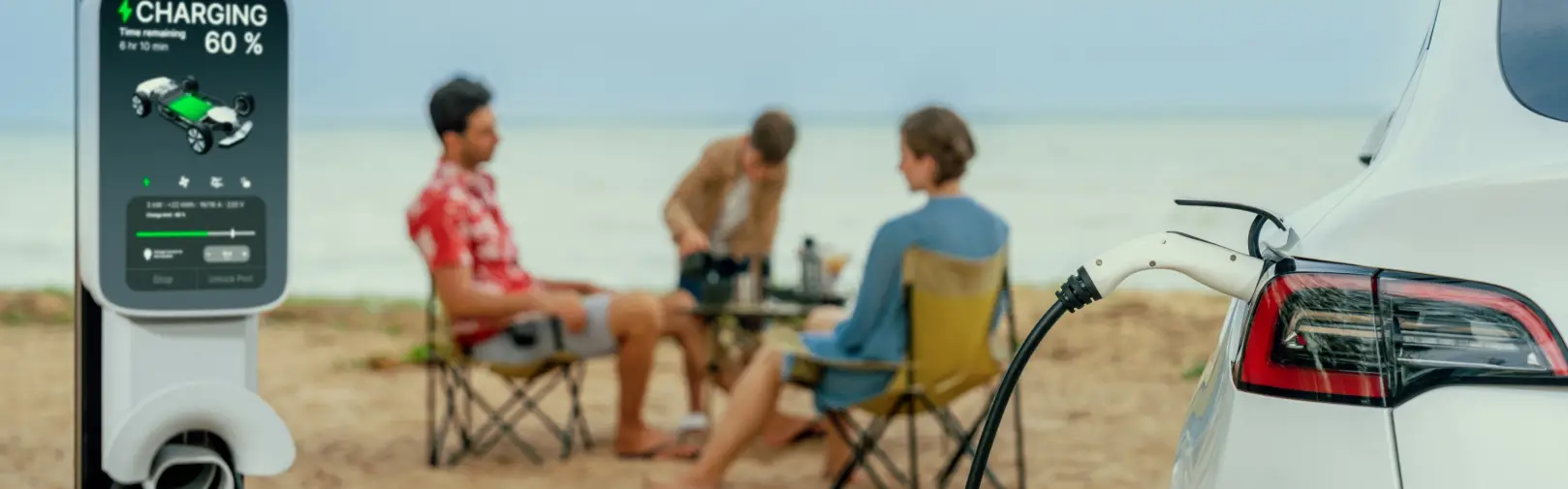An electric car plugged into a charging post reading 60 per cent, people sitting in beach chairs on the sand behind
