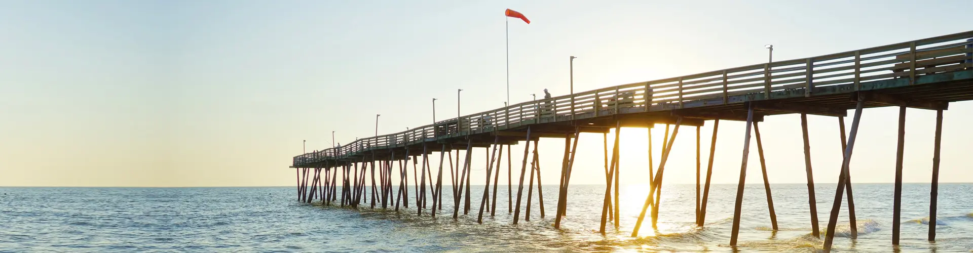 A long wooden fishing pier running out over calm water in warm golden evening light