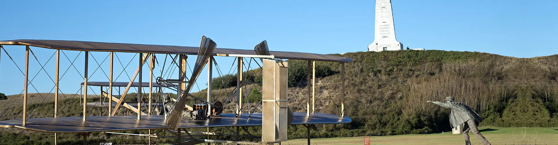 A replica of the Wright brothers' 1903 Flyer on its launching rail, the granite Wright Brothers Memorial on the hill behind