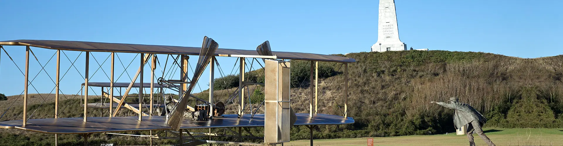 A replica of the Wright brothers' 1903 Flyer on its launching rail, the granite Wright Brothers Memorial on the hill behind