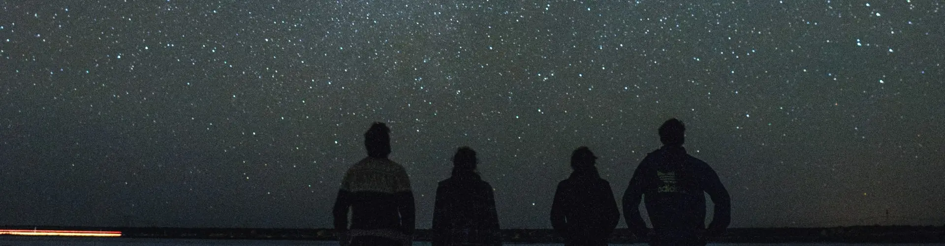 Four figures silhouetted against a night sky thick with stars