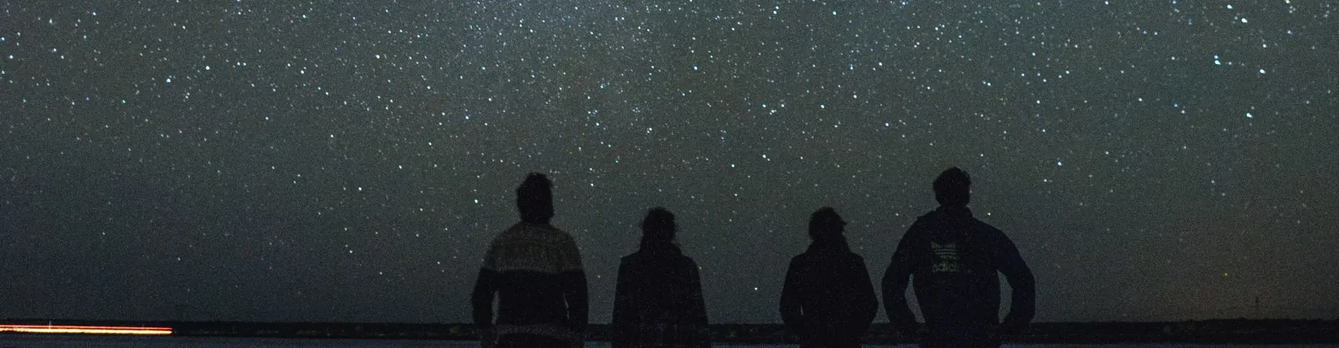 Four figures silhouetted against a night sky thick with stars