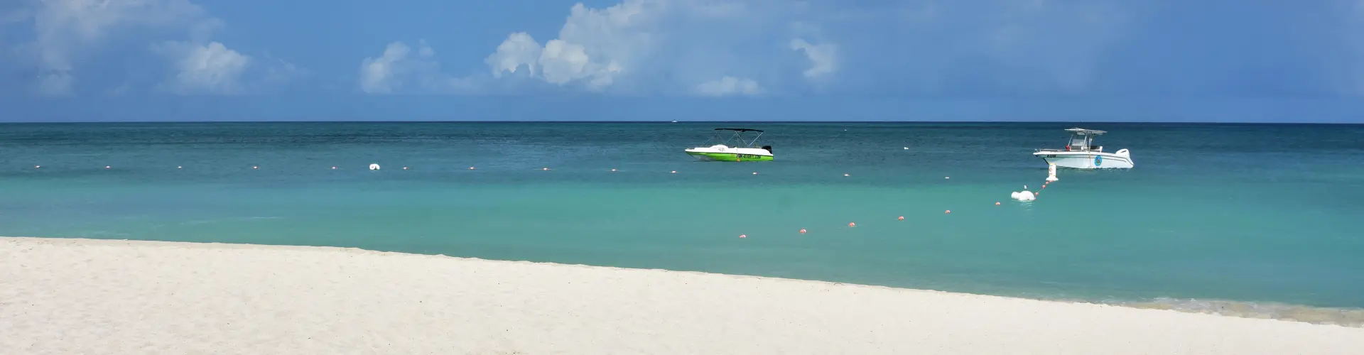 Two small boats moored on flat turquoise water off an empty white sand beach under a clear sky