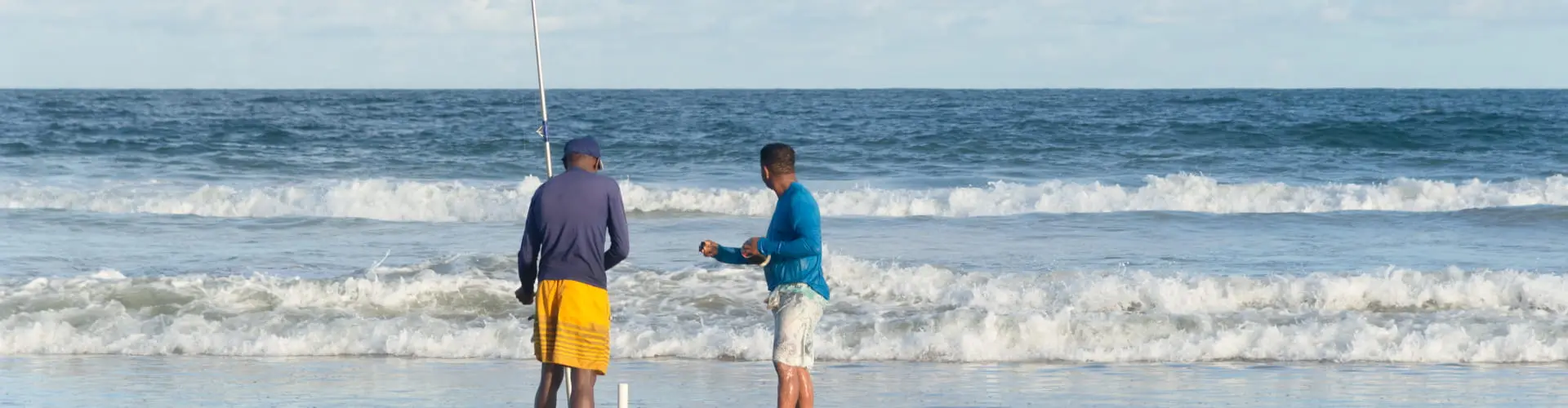 Two surf anglers standing in the shallows with rods raised as a wave breaks behind them