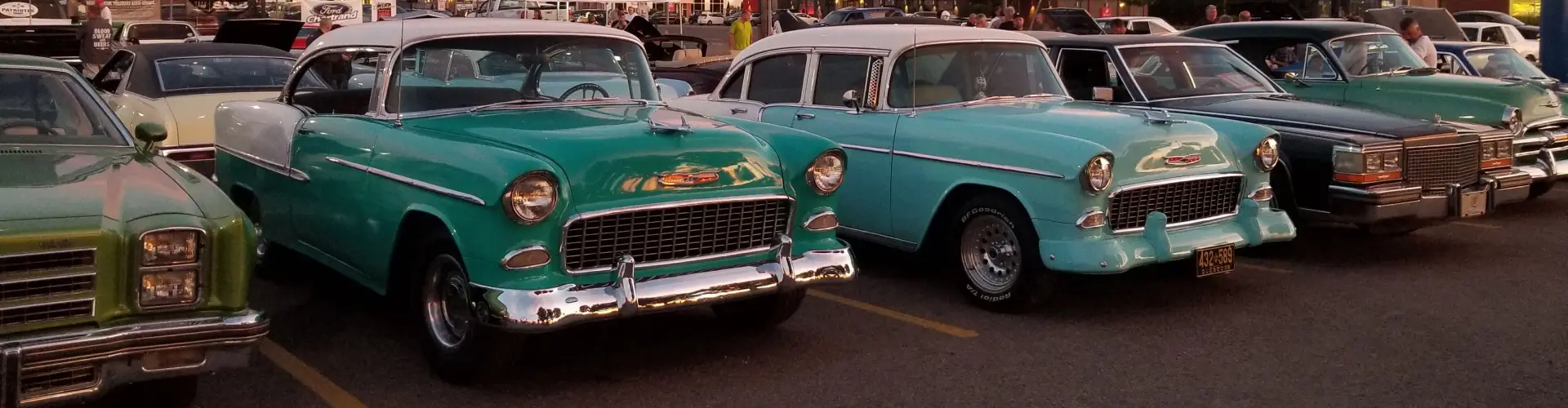 A row of polished 1950s cars parked nose-out at a classic car show, a turquoise Chevrolet in the middle