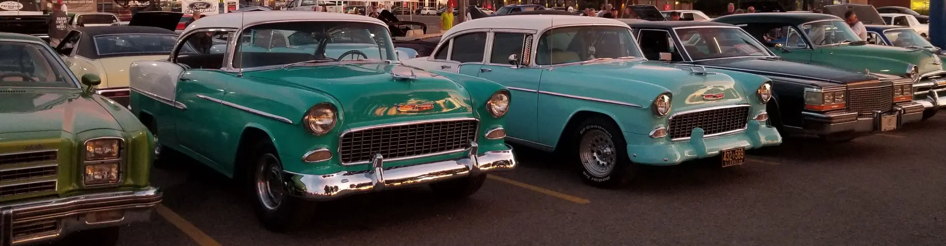 A row of polished 1950s cars parked nose-out at a classic car show, a turquoise Chevrolet in the middle