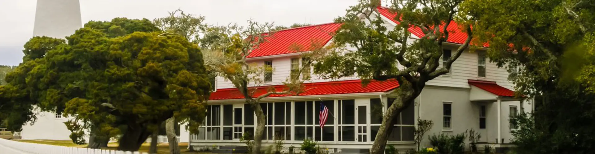 A white clapboard house with a red metal roof shaded by big spreading live oaks