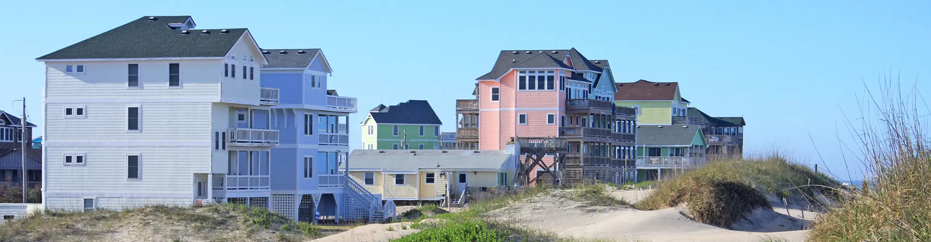 Pastel-painted beach houses on stilts crowded behind low dunes under a bright blue sky