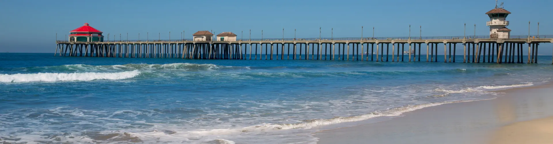 An empty stretch of sand with a long pier and its pier house reaching out over clear turquoise surf