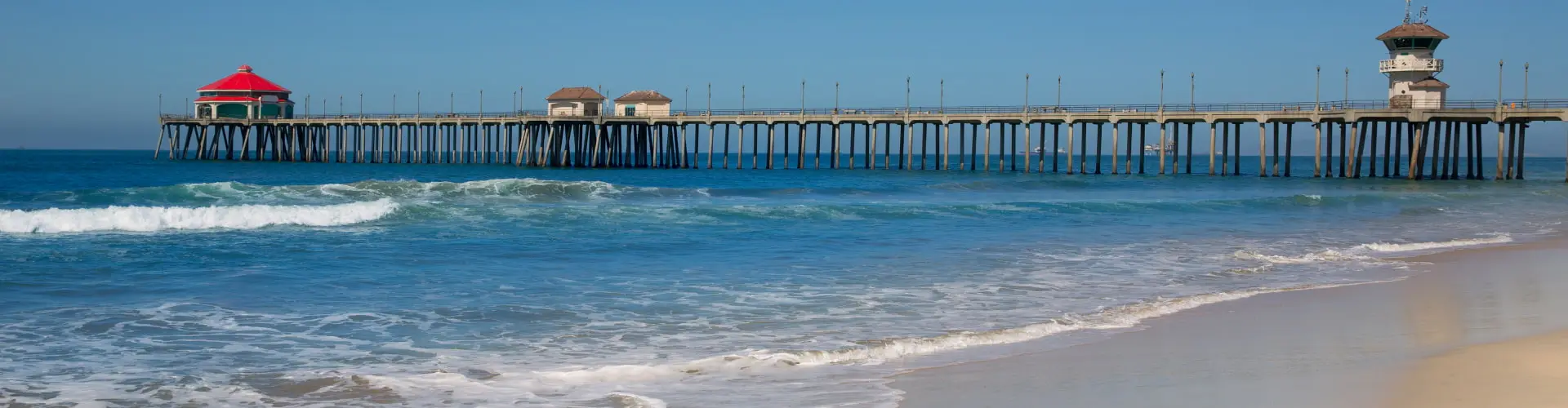 An empty stretch of sand with a long pier and its pier house reaching out over clear turquoise surf