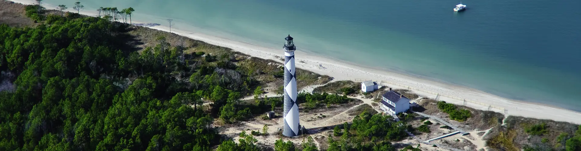 Cape Lookout Lighthouse and its keeper's house from the air, black-and-white diamonds above maritime forest, white sand and turquoise water