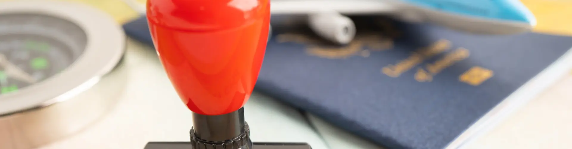 A red rubber stamp resting on an open passport beside a compass