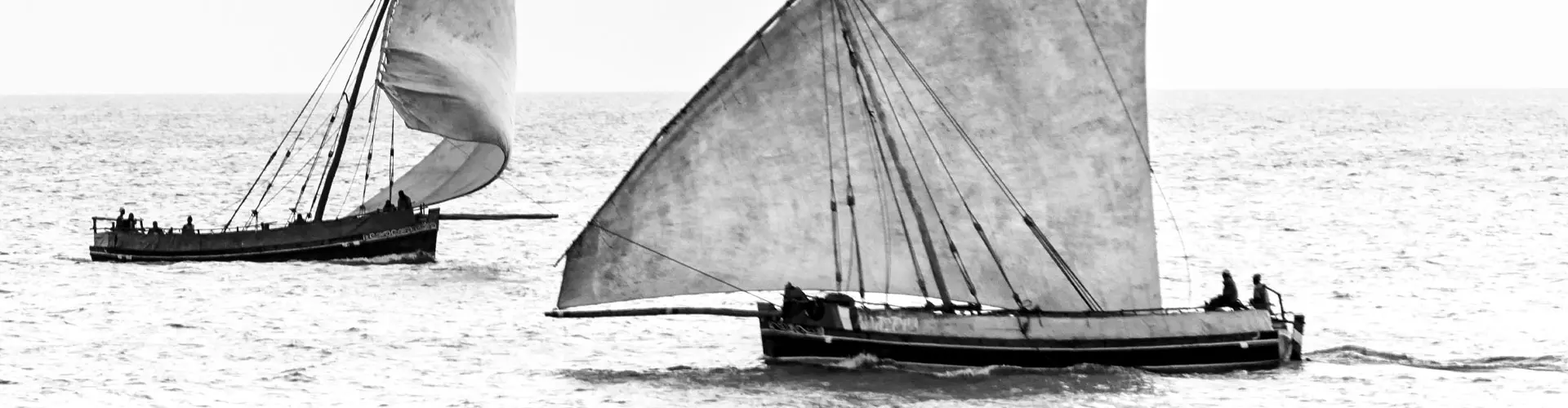 An old black and white photograph of small wooden sailing boats drawn up in shallow water
