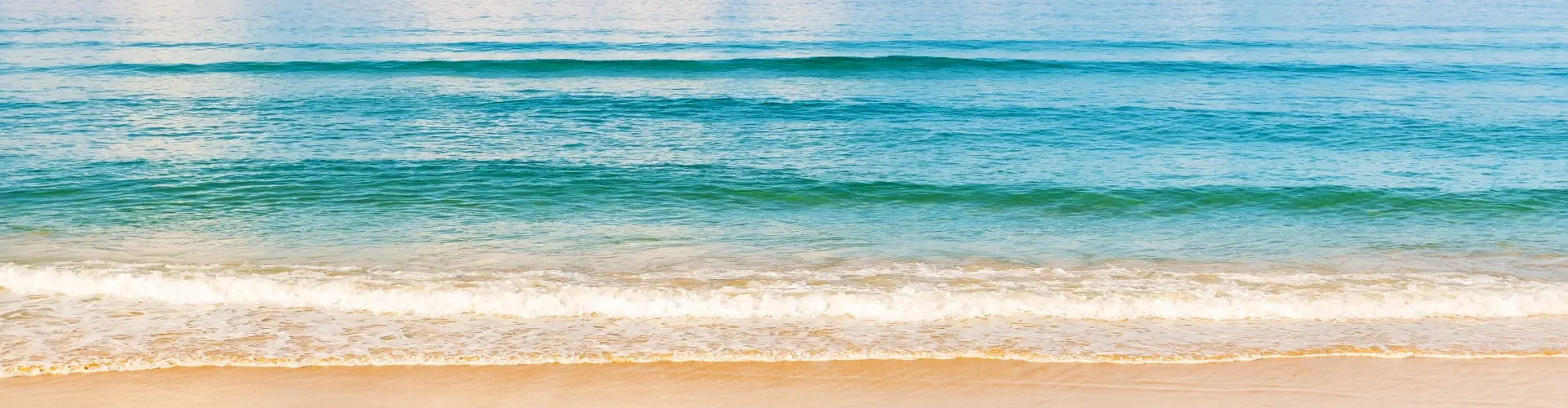 Bands of turquoise and deep blue water rolling in over pale sand, seen from above