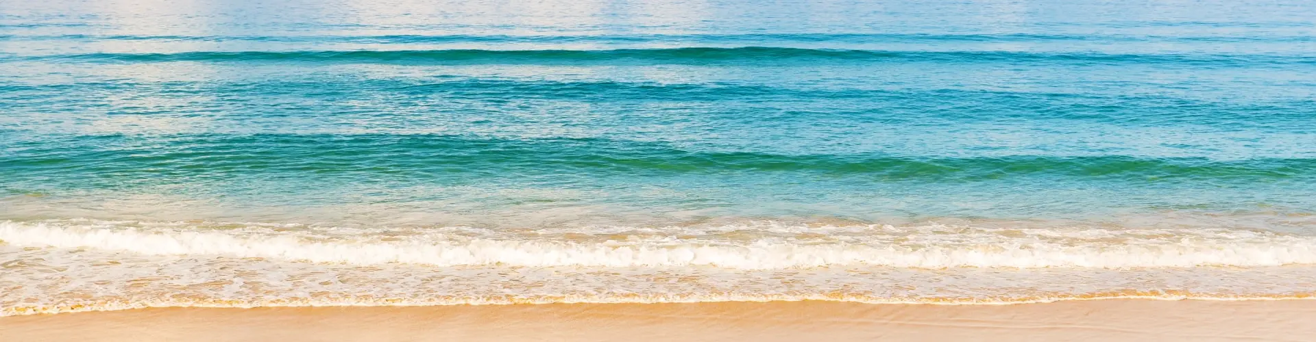 Bands of turquoise and deep blue water rolling in over pale sand, seen from above