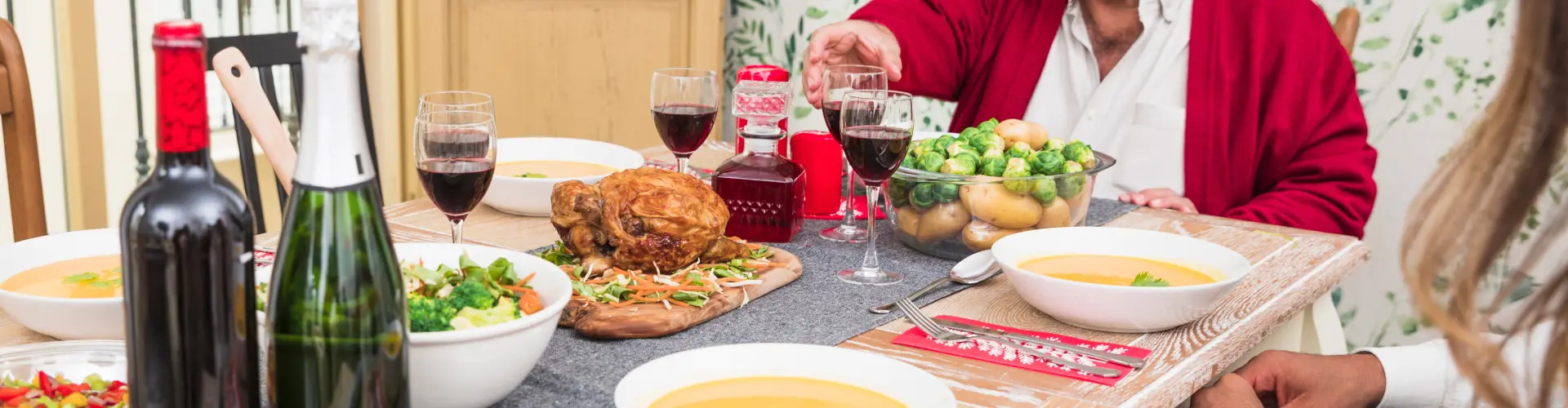 People raising glasses of red wine over a laden table of roast food and bottles