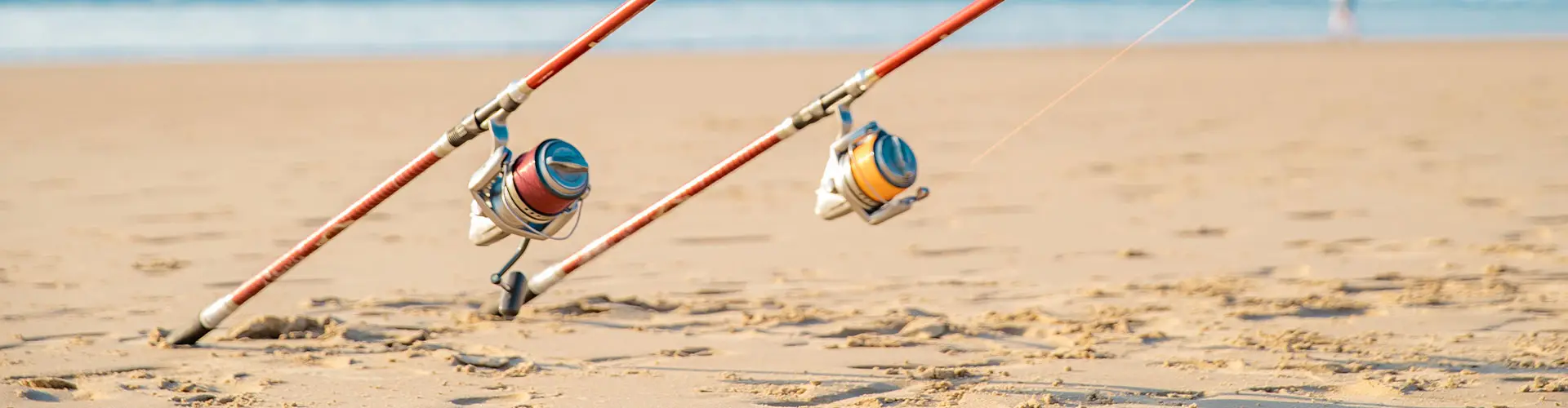Two surf-fishing rods with their reels resting on the sand, lines running out of frame