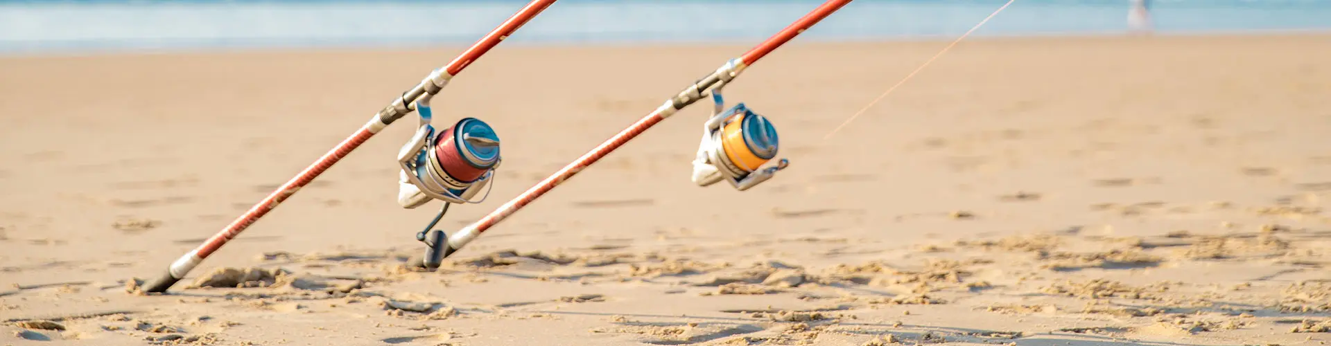 Two surf-fishing rods with their reels resting on the sand, lines running out of frame