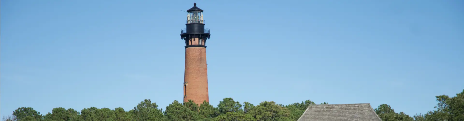 Currituck Beach Lighthouse, an unpainted red-brick tower with a black lantern room, rising above maritime forest