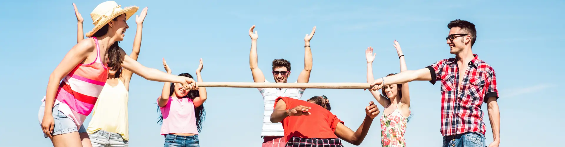 A line of young people in summer clothes on the beach, arms linked and raised together