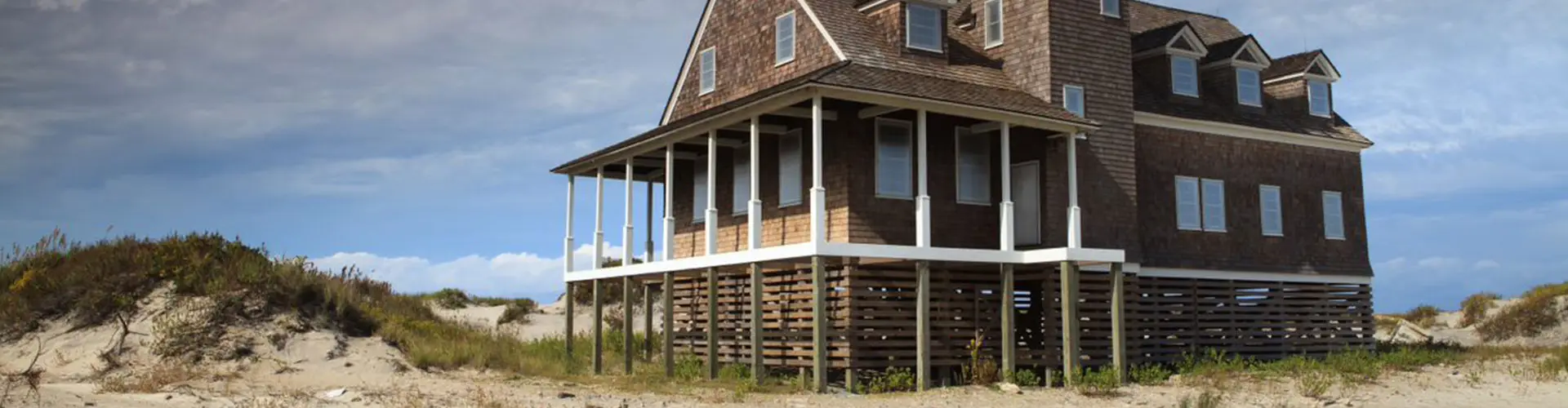 A weathered dark-shingled house with deep porches standing alone on the dunes