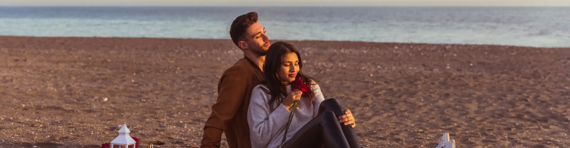 A couple sitting close together on the sand in low golden light