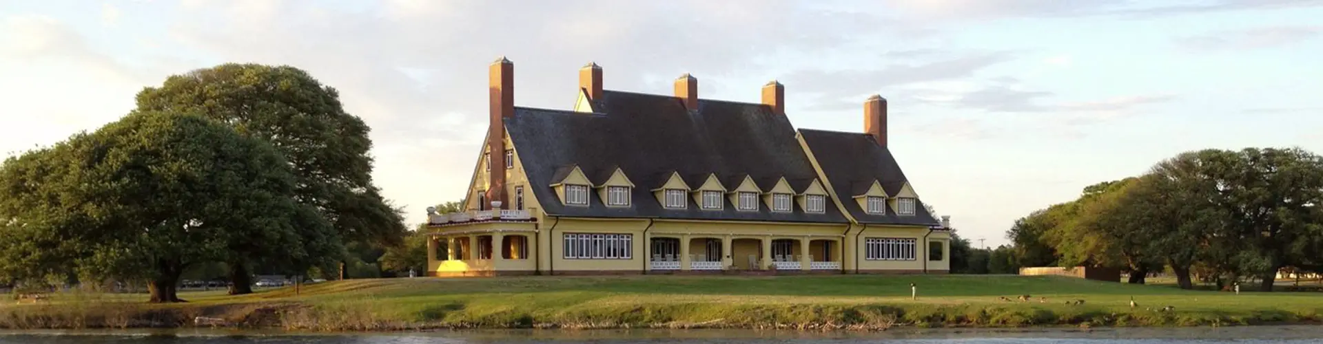 The yellow gambrel-roofed Whalehead house with its brick chimneys, seen across the lawn under a broad oak
