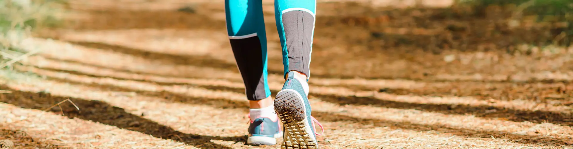 Close on a walker's legs and trainers on a bare sandy trail
