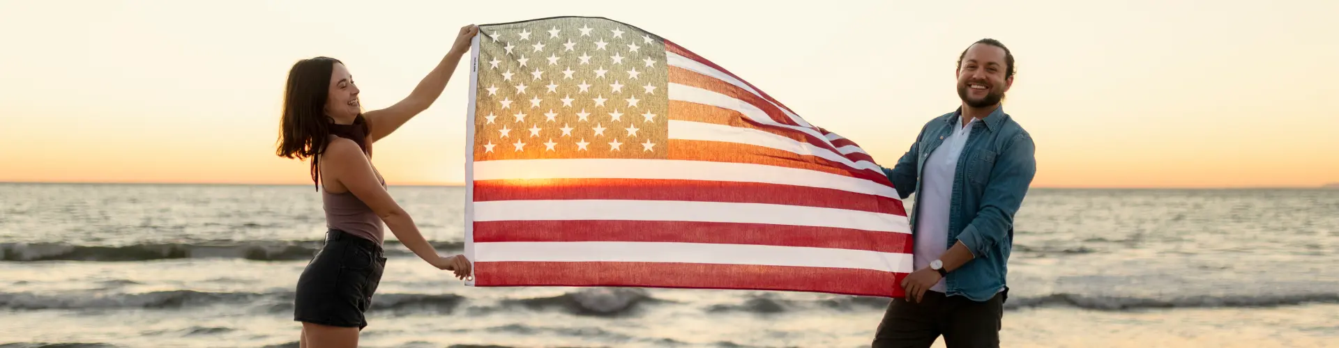 A couple holding an American flag stretched open between them on the beach at sunset