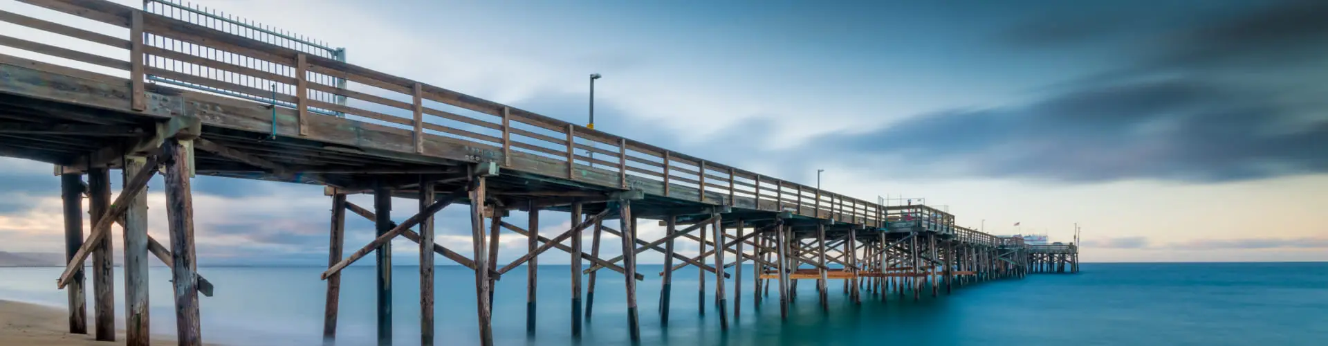 A long fishing pier on wooden pilings reaching out over still water at dusk