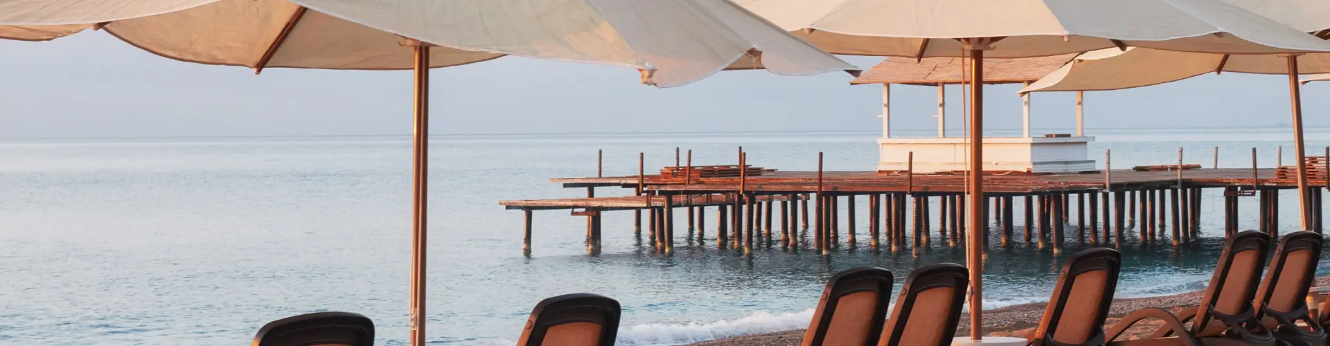 Sun loungers under canvas umbrellas on a jetty over flat blue water