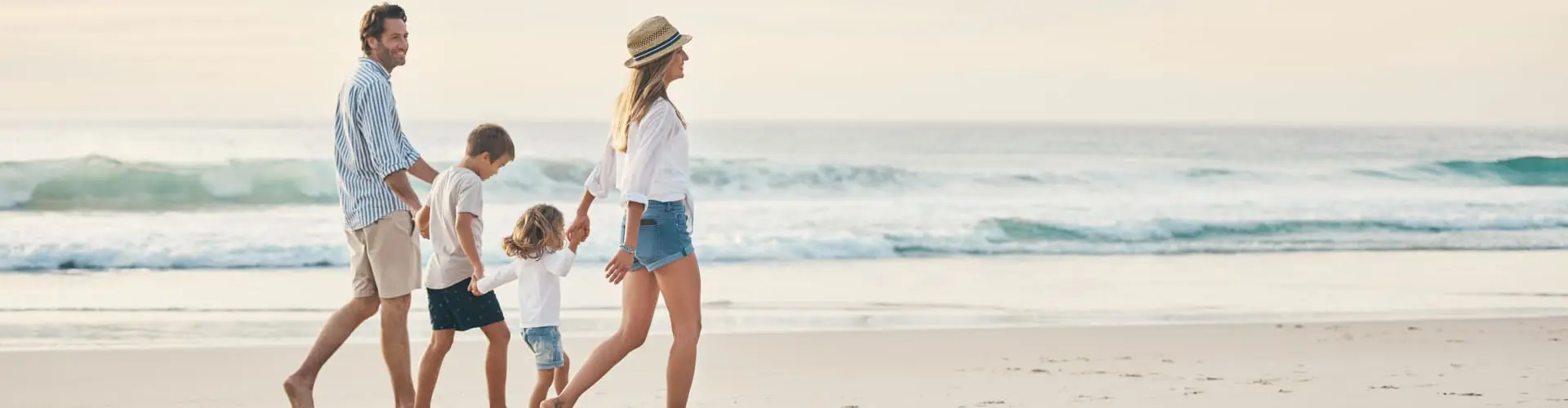 A family of four walking away along the sand, the surf breaking beside them