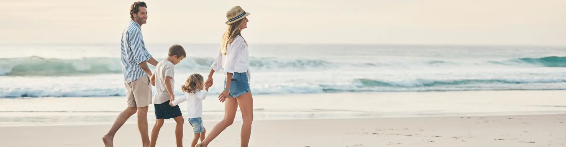 A family of four walking away along the sand, the surf breaking beside them