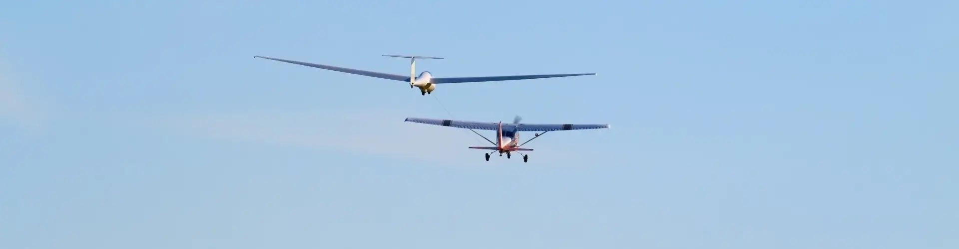 A small light aircraft and a glider flying together high in a clear blue sky